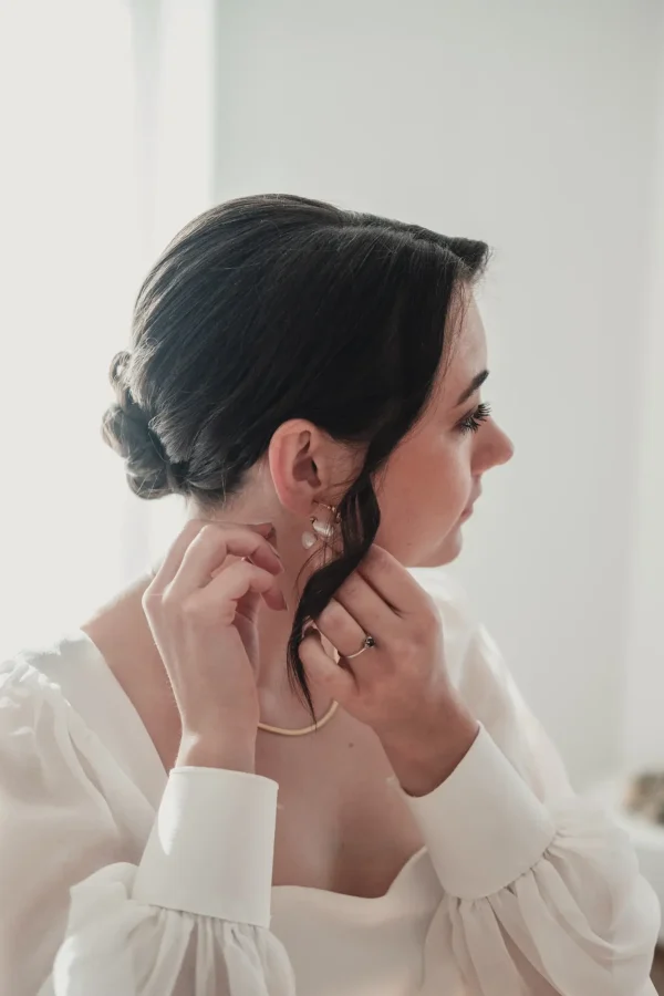 Nahaufnahme der Braut beim Anlegen ihrer Ohrringe, ein ruhiger Moment vor der Trauung.