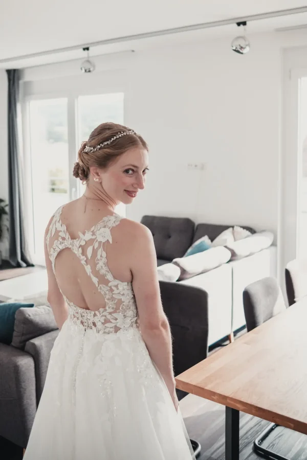 Rückansicht der Braut, die ihr prachtvolles, mit floraler Spitze verziertes Kleid präsentiert – ein strahlender Moment der Ruhe vor der Trauung.