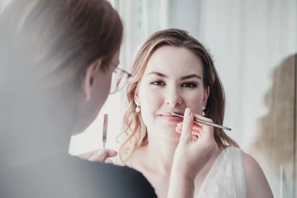 Detailaufnahme des Brautstylings, Visagistin trägt Lippenstift auf