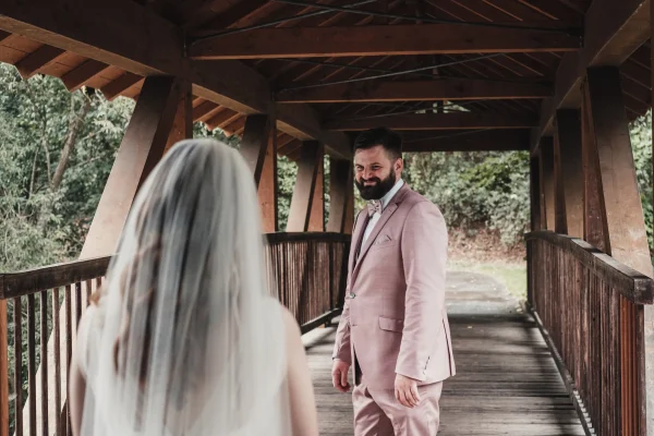 Bräutigam lächelt seine Braut an, als sie sich auf der Holzbrücke zum ersten Mal sehen