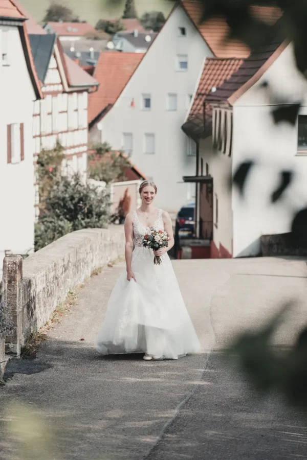 Braut im weißen Hochzeitskleid mit Blumenstrauß auf einer idyllischen Straße in Murrtal während des First Looks bei der Hochzeit auf Burg Reichenberg