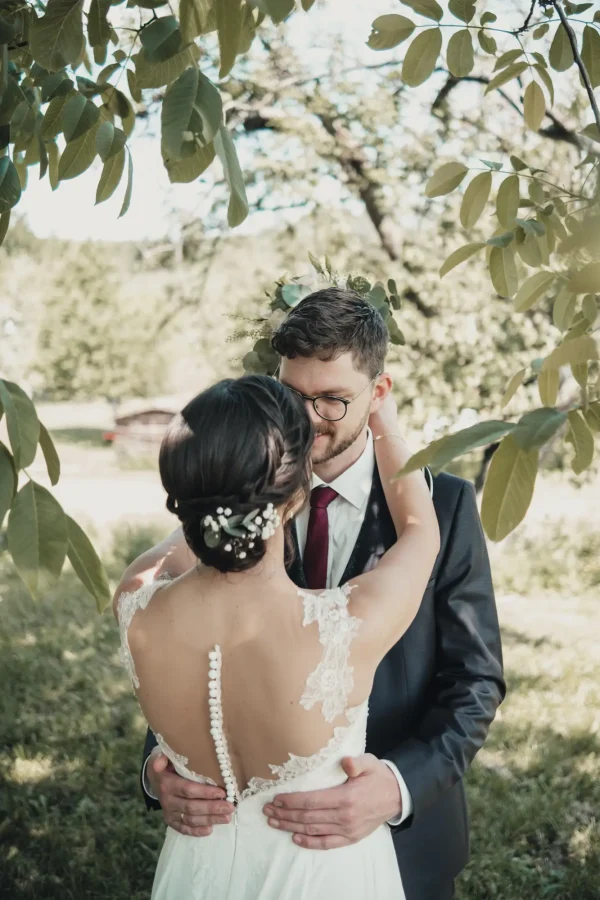 Das Brautpaar genießt ihren besonderen Tag – ein verliebter Blick und zärtliche Geste unter einem Baum auf einer Sommerhochzeit in Mötzingen.