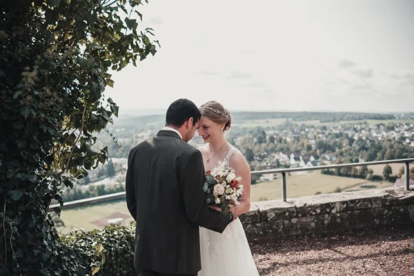 Das Brautpaar beim First Look umgeben von einer malerischen Landschaft mit sanften Hügeln und einem strahlend blauen Himmel. Die Braut hält ihren Blumenstrauß und schaut ihren Bräutigam liebevoll an