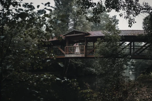 Verliebter Blick des Bräutigams zur Braut beim First Look auf der Holzbrücke