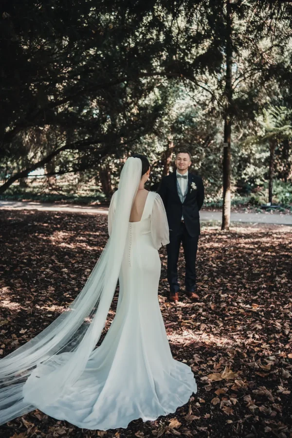 Die Braut geht auf den Bräutigam zu, ihr langer Schleier fließt über den herbstlichen Waldboden. Eine zauberhafte Szene inmitten der Natur des Hohenheimer Parks.