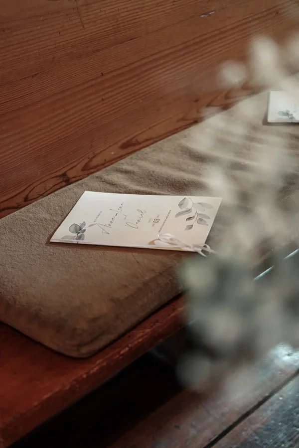 Individuell gestaltetes Kirchenheft mit floralem Design liegt auf einer gepolsterten Holzbank in der Mauritiuskirche Mötzingen.