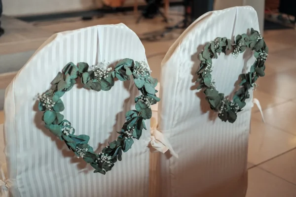 Romantische Hochzeitsdekoration: Zwei mit Eukalyptus und Schleierkraut verzierte Herzkränze schmücken die Stuhlhussen im Traubereich.