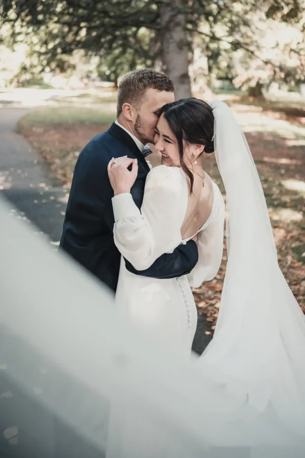 Brautpaar im Hohenheimer Park, Schleier der Braut führt ins Bild. Der Bräutigam flüstert ihr etwas ins Ohr