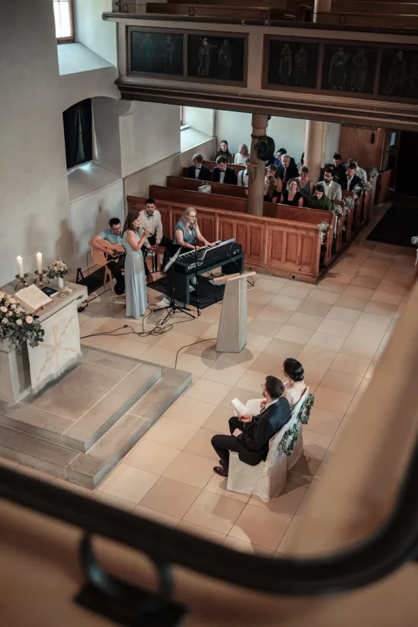 Blick von der Empore in die Mauritiuskirche Mötzingen: Musiker begleiten die Trauung von Ena & Daniel mit Live-Musik, während das Brautpaar vorne sitzt.