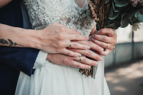 Detailaufnahme von Strauß und Händen des Brautpaars. Eheringe und Tattoo der Braut sichtbar