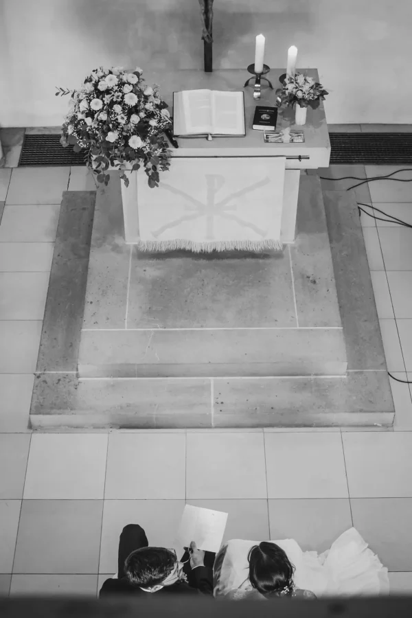 Blick von oben auf den Altar der Mauritiuskirche Mötzingen mit aufgeschlagener Bibel, Kerzen und Blumenarrangements, während Mann und Frau ihr Eheversprechen lesen.