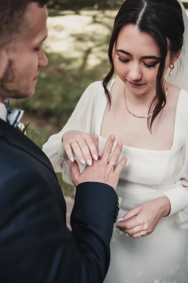 Die Braut betrachtet liebevoll die Hand des Bräutigams, während sie ihren Ehering berührt. Eine intime Nahaufnahme des Moments nach der Trauung, voller Emotion und Bedeutung.