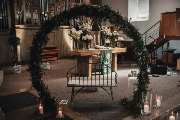 Stimmungsvolle Dekoration in der Martinskirche: Ein mit Olivenzweigen geschmückter Traubogen steht vor dem festlich geschmückten Altar. Weiße Blumen, Kerzen und eine warme Lichtstimmung schaffen eine besondere Atmosphäre für die Trauung.