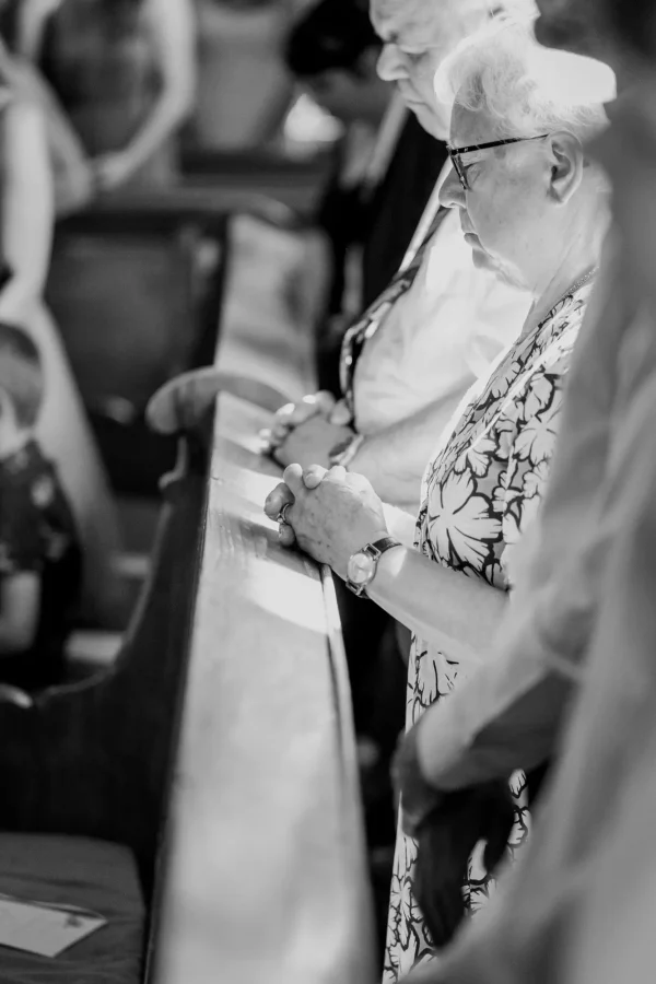 Nachdenkliche Hochzeitsgäste in der Mauritiuskirche Mötzingen, die mit gefalteten Händen beten und den feierlichen Moment genießen.