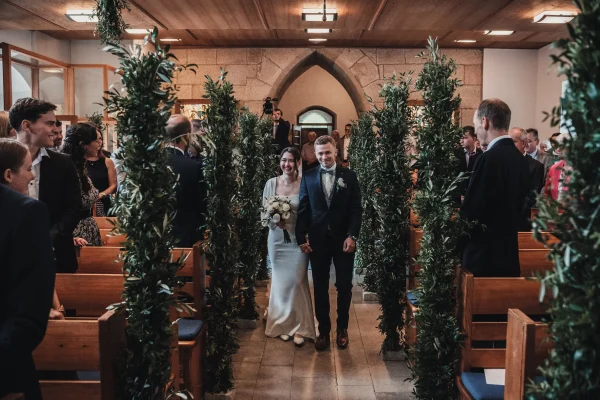 Der feierliche Auszug des Brautpaares aus der Martinskirche: Hand in Hand schreiten sie durch den mit Olivenzweigen geschmückten Mittelgang, während die Gäste sie voller Freude betrachten. Ein symbolischer Moment voller Glück.