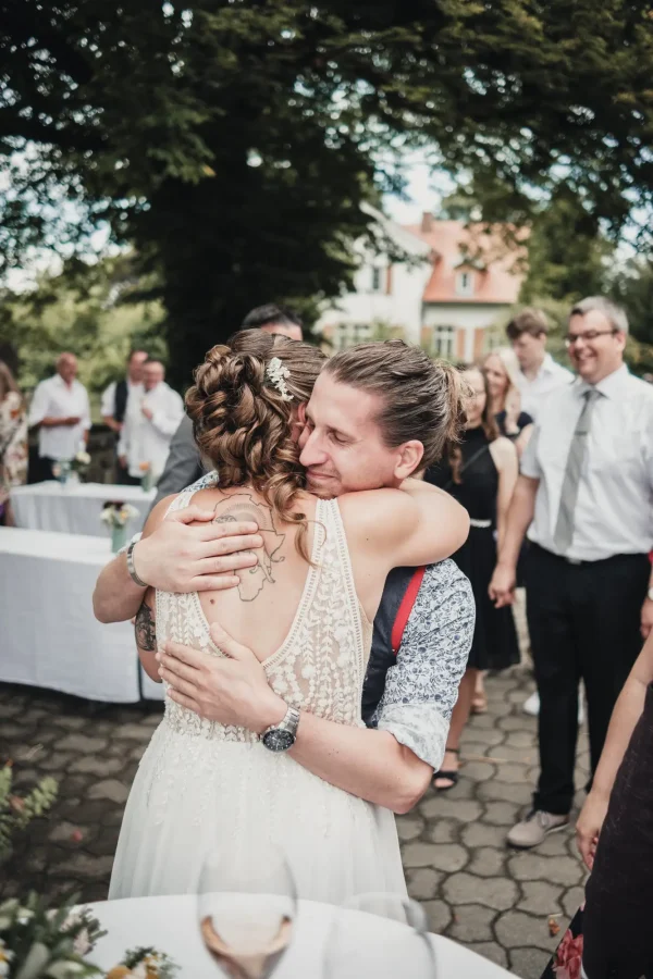 Hochzeitsgäste umarmen das Brautpaar unter strahlendem Himmel, Freude und Liebe in der Luft.