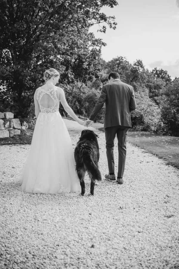 Das Brautpaar spaziert Hand in Hand mit ihrem Berner Sennenhund über einen Kiesweg, eine ländliche Kulisse im Hintergrund.