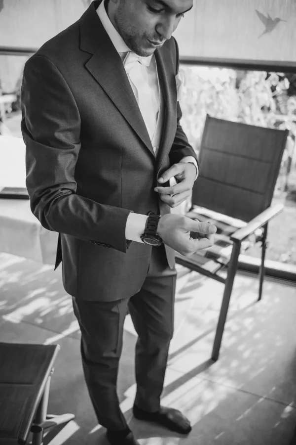 Der Bräutigam prüft die Details seines eleganten Anzugs, festgehalten in einem natürlichen Schwarz-Weiß-Stil während des Getting Ready.
