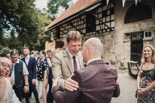 Herzliches Lachen des Trauzeugen beim Sektempfang mit Bräutigam.