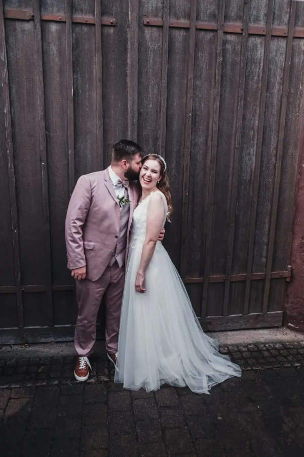 Der Bräutigam küsst seine Braut zärtlich an einer rustikalen Holzwand