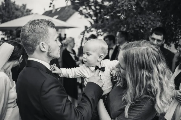 Ein Kleinkind gratuliert dem Bräutigam und fasst ihm an die Fliege.