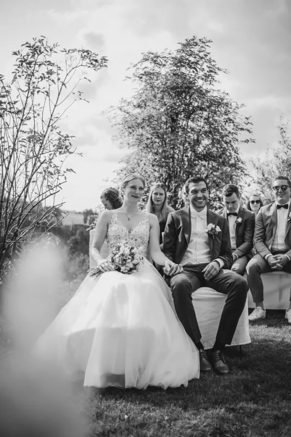 Das Brautpaar sitzt während der freien Trauung auf weißen Stühlen im Außengelände des Lana Salta. Die Braut lächelt liebevoll, während der Bräutigam voller Freude in die Runde blickt.