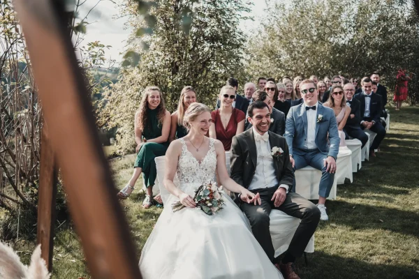 Das Brautpaar hält sich während der Trauung an den Händen. Im Hintergrund sind die Gäste und die natürliche Kulisse des Lana Salta zu sehen.