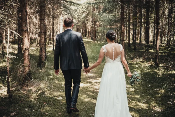 Hochzeitspaar spaziert Arm in Arm durch einen Waldweg – natürliche und intime Hochzeitsfotografie inmitten der Natur.
