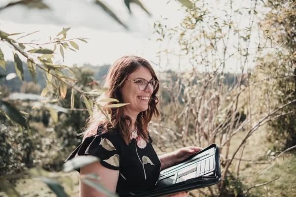 Jasmin von „100 Dinge an dir“ hält die freie Trauung mit einem Lächeln und einer Mappe in der Hand. Der Traubogen im Hintergrund ergänzt die natürliche Kulisse des Lana Salta.