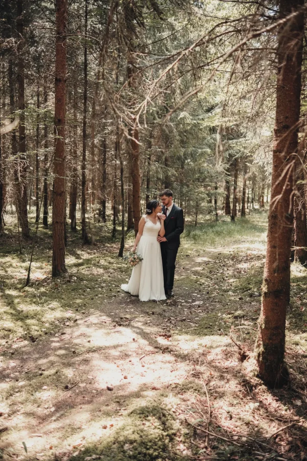 Hochzeitspaar steht eng umschlungen in einem lichten Wald – romantische und natürliche Hochzeitsaufnahme mit weichem Lichtspiel.