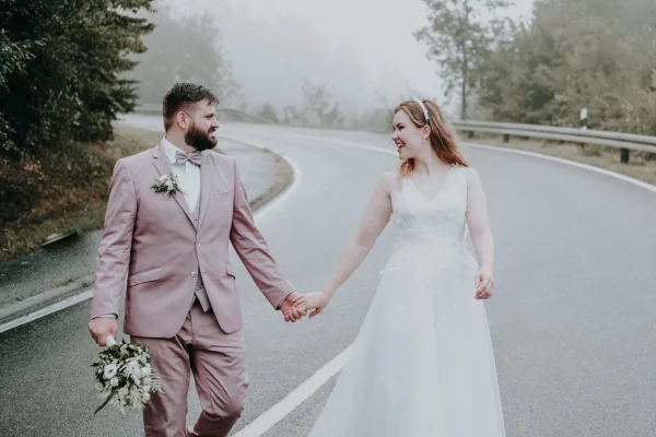 Das Brautpaar geht Hand in Hand die neblige Landstraße im Schwarzwald entlang