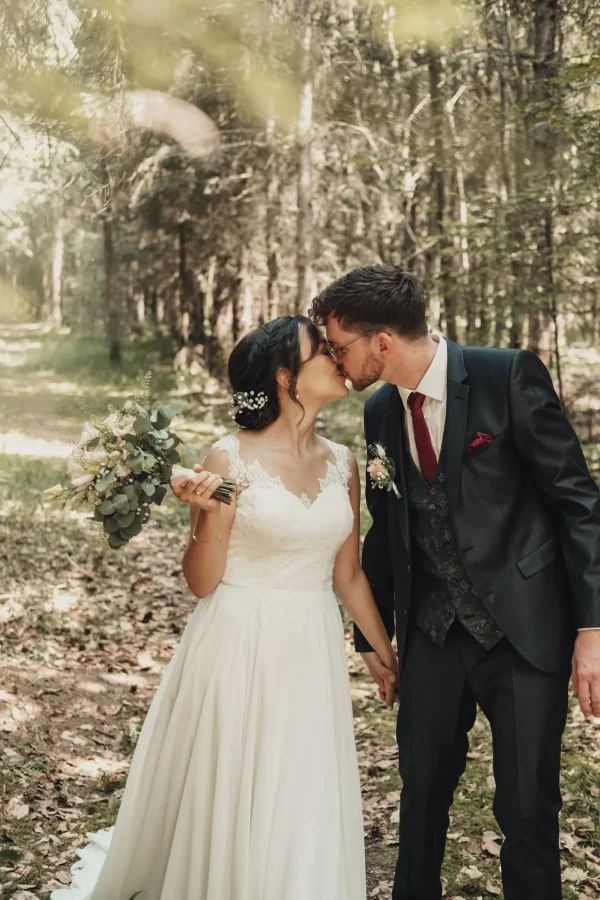 Kuss des Hpchzeitspaares im Wald. Blätter im Vordergrund.