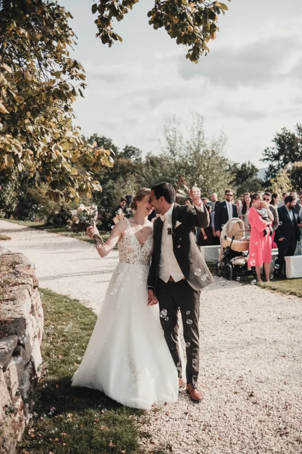 Jubelnder Auszug mit Seifenblasen nach der Trauung. Die Braut hält den Blumenstrauß jubelnd in die Luft