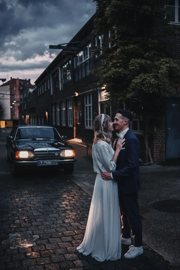 Stimmungsvolle Abendaufnahme im Innenhof des Wizemann. Mercedes Oldtimer beleuchtet das zugewandte Brautpaar im Vordergrund.