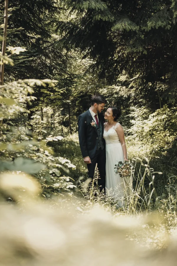 Brautpaar beim Fotoshootimg im Wald. Umgeben von Bäumen und sattem Grün.