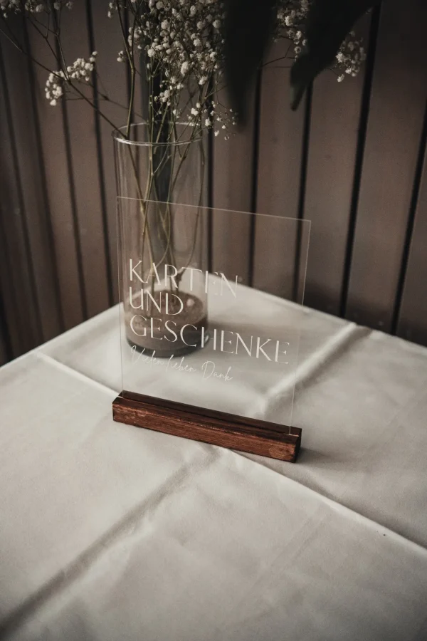 Elegantes Acrylschild mit der Aufschrift „Karten und Geschenke – Vielen lieben Dank“, aufgestellt auf einem Tisch mit weißer Tischdecke, dekoriert mit einer Vase voller Schleierkraut.