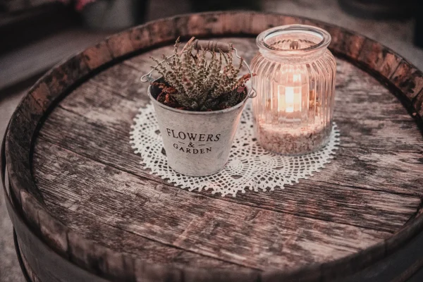 Eine stilvolle Hochzeitsdekoration auf einem alten Weinfass – ein Zinktopf mit Sukkulente, eine gehäkelte Spitzendecke und eine leuchtende Kerze im Glas sorgen für gemütliche Atmosphäre.