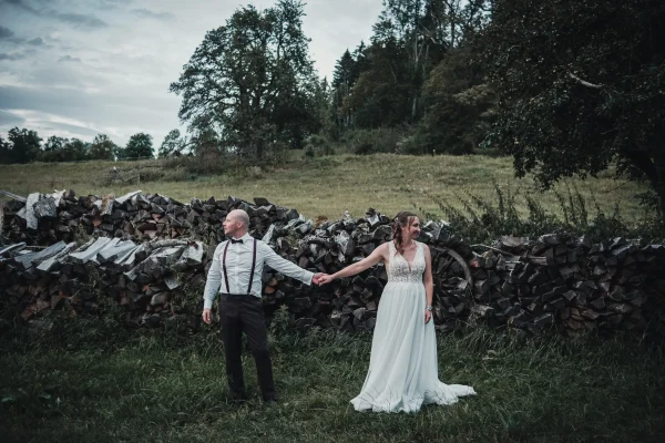Brautpaarshooting abends auf einer Wiese vor Holzstapeln.