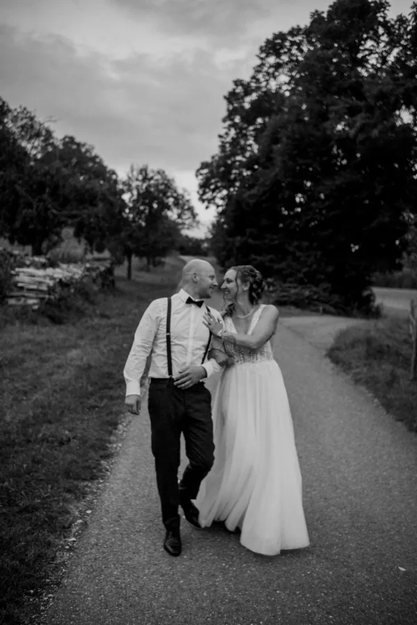 Das Brautpaar spaziert Hand in Hand zurück zur Feier nach dem Abendshooting auf dem Feldweg.