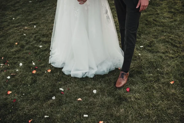 Detailaufnahme der Füße und des Brautkleids auf der Rasenfläche mit bunten Rosenblättern