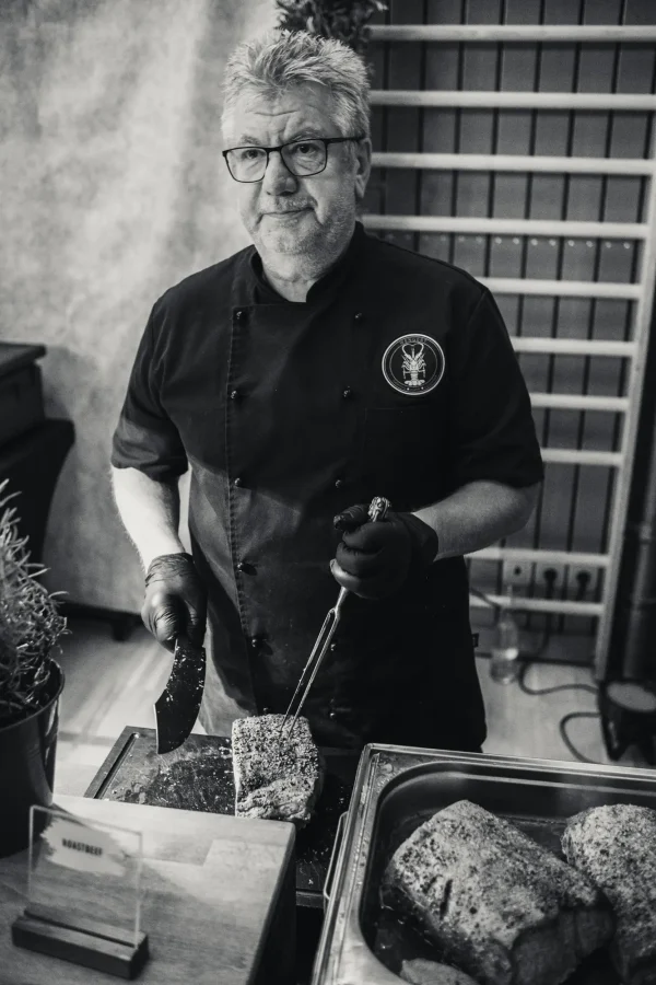 Nahaufnahme eines Kochs, der ein perfekt gegartes Stück Roastbeef mit einer Zange hält und mit einem scharfen Messer in Scheiben schneidet.