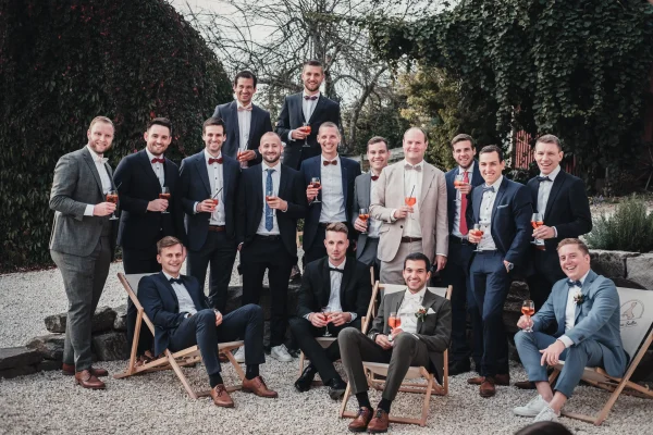 Der Bräutigam und seine Freunde auf einem modernen Gruppenbild mit Liegestühlen, Kies und Aperolgläsern in der Hand