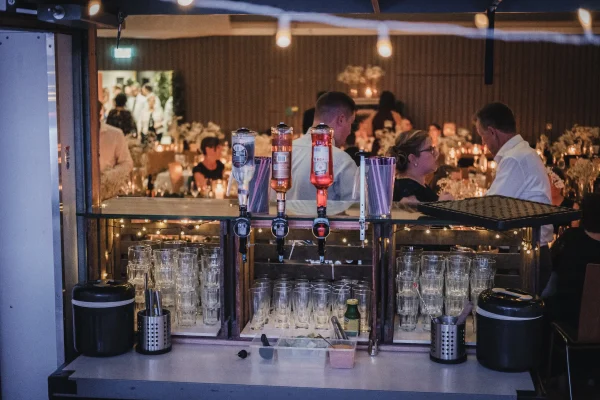 Cocktailbar mit Flaschen und Gläsern. Gäste im Hintergrund.