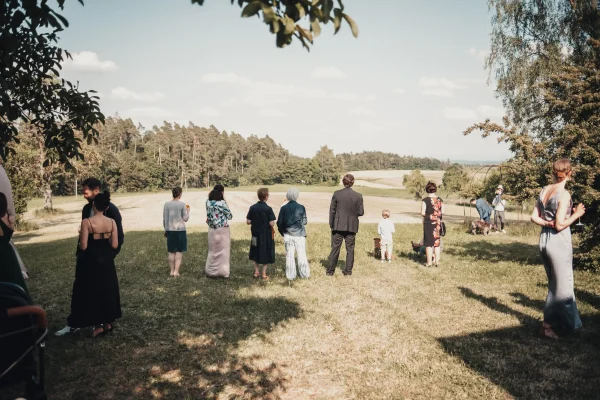 Blick auf die Hochzeitsgesellschaft. Gäste stehen unter Bäumen und schauen in die Weite.