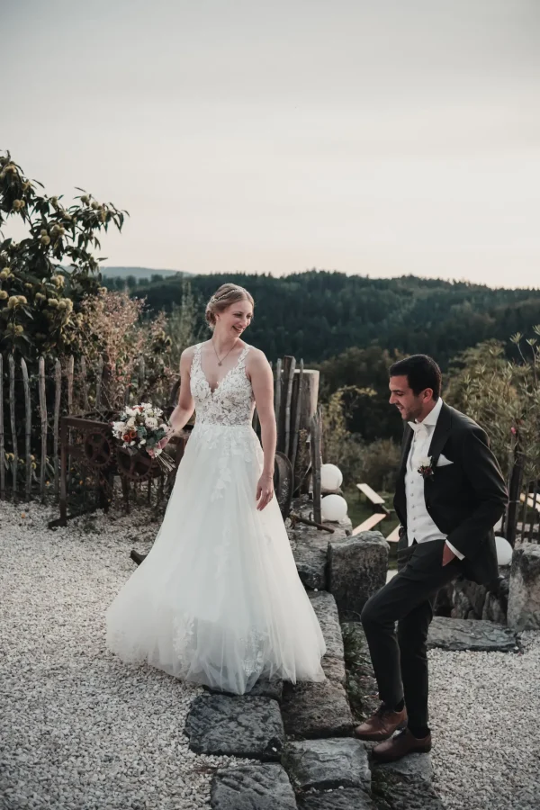 Das Paar posiert auf einer Treppe. Holzzaun und Wald im Hintergrund.