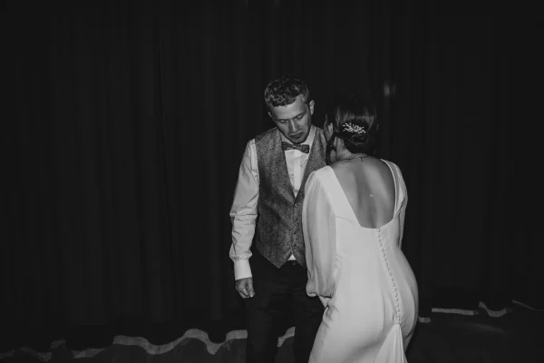 Schwarz-Weiß-Fotografie des Brautpaares auf der Tanzfläche, die Braut mit dem Rücken zur Kamera, während der Bräutigam nachdenklich nach unten blickt. Der dunkle Vorhang im Hintergrund erzeugt eine intime Atmosphäre.