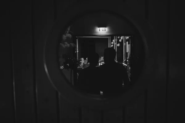 Silhouetten des Brautpaares in einem runden Türfenster, während sie gemeinsam den Festsaal verlassen. Stimmungsvolle Beleuchtung und festliche Dekoration im Hintergrund.