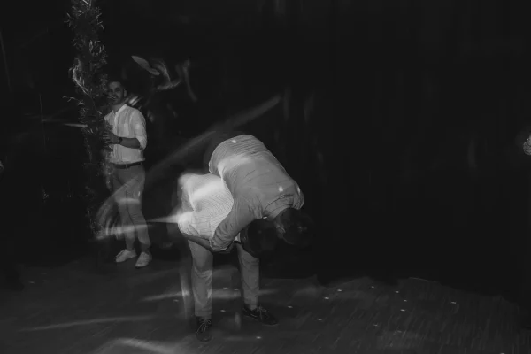 Schwarz-Weiß-Fotografie einer ausgelassenen Feier: Ein Gast hebt einen Freund spielerisch hoch, während die Lichter der Tanzfläche für eine energiegeladene Stimmung sorgen.