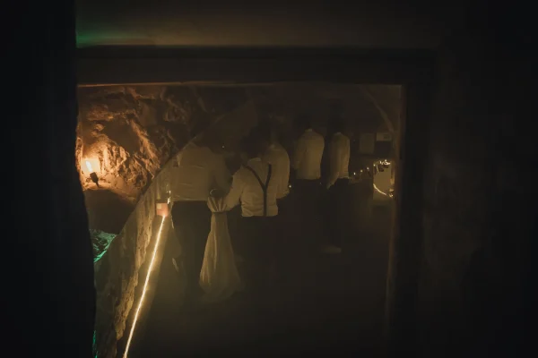 Der Partykeller mit Baar, männliche Gäste ihn Anzug und Hosenträgern im Gespräch an der Bar.